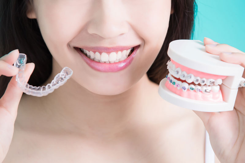 Invisalign Patient Smiling While Holding A Braces Model and Invisalign Clear Retainers