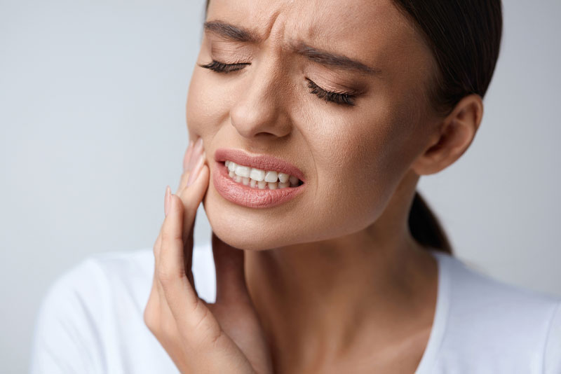 a picture of a woman who needs emergency dentistry as she holds her jaw in pain.