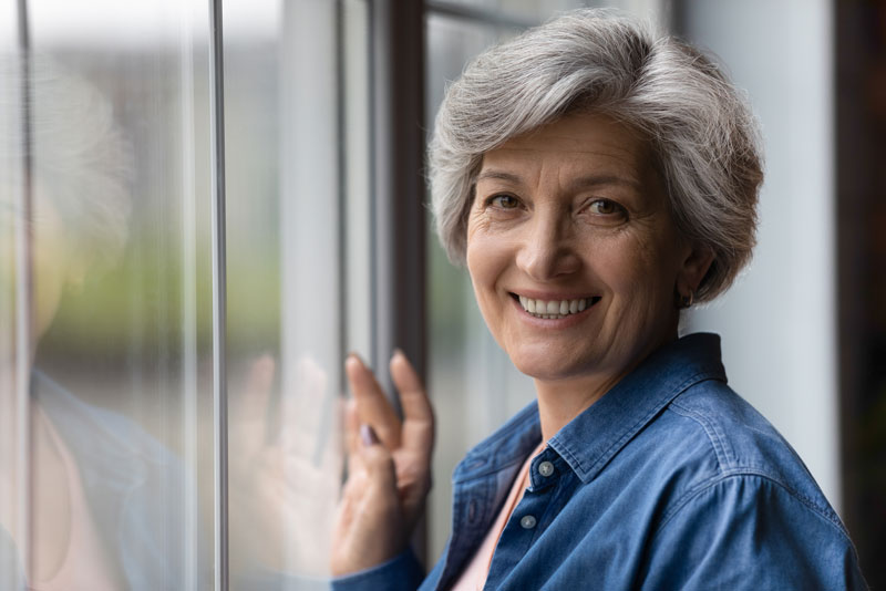 a full mouth dental implant patient smiling by a window.